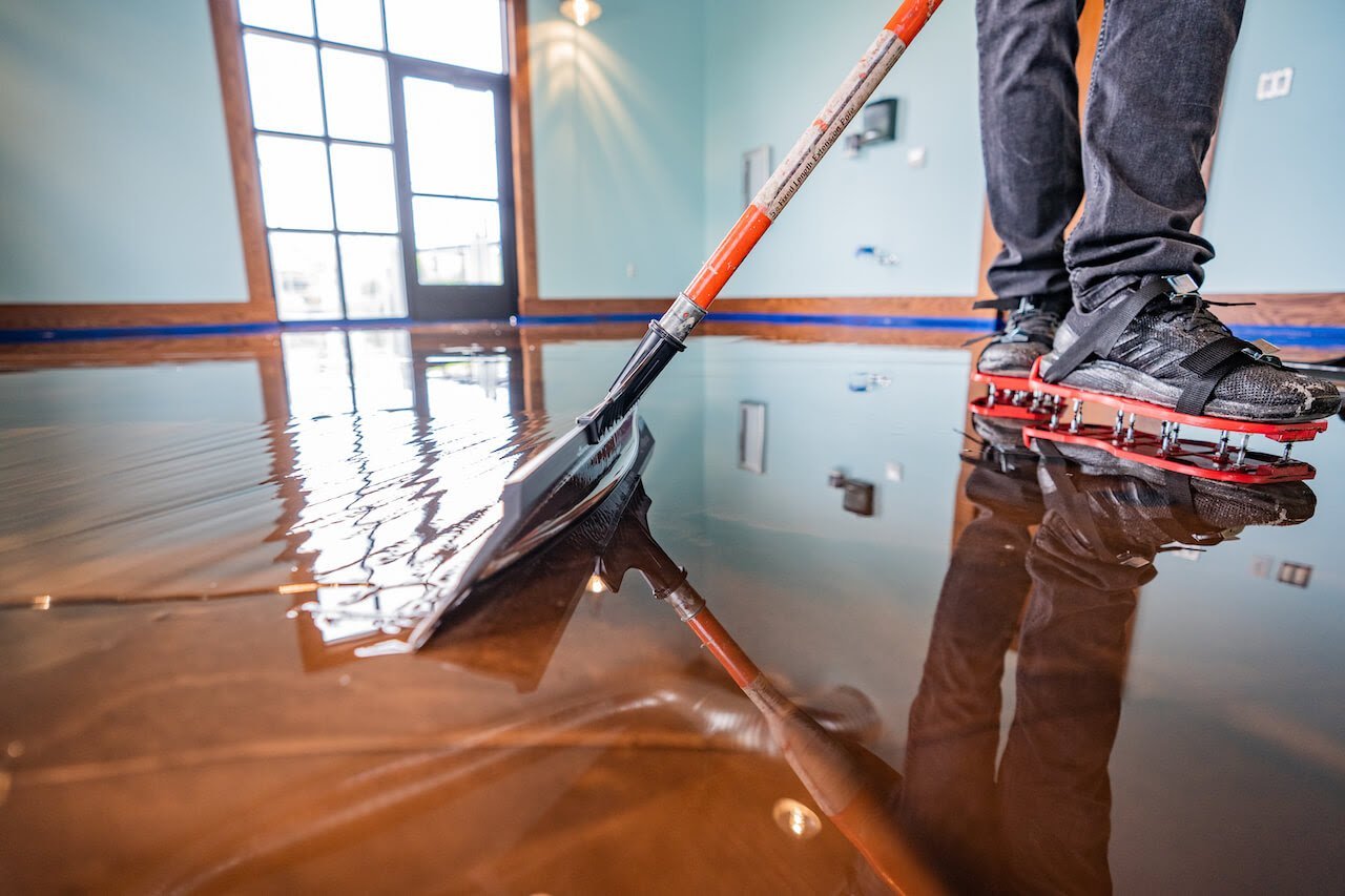 Person with squeegee removing floodwater from interior floor with large window reflection visible